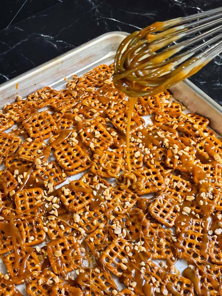 Butter toffee being drizzled over the pretzels in a baking sheet.