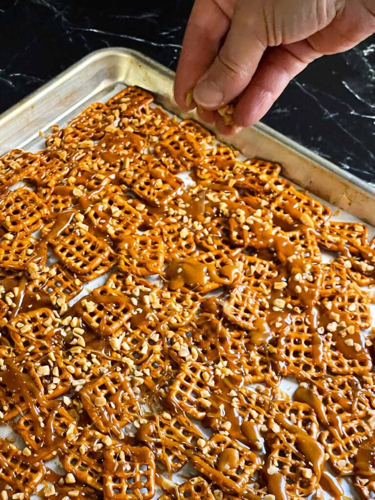 Sprinkling toffee bits over the warm drizzled toffee on the pretzels.