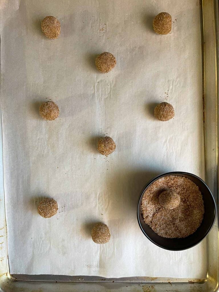 Chai sugar cookie dough balls rolled in chai sugar on a parchment lined baking sheet.