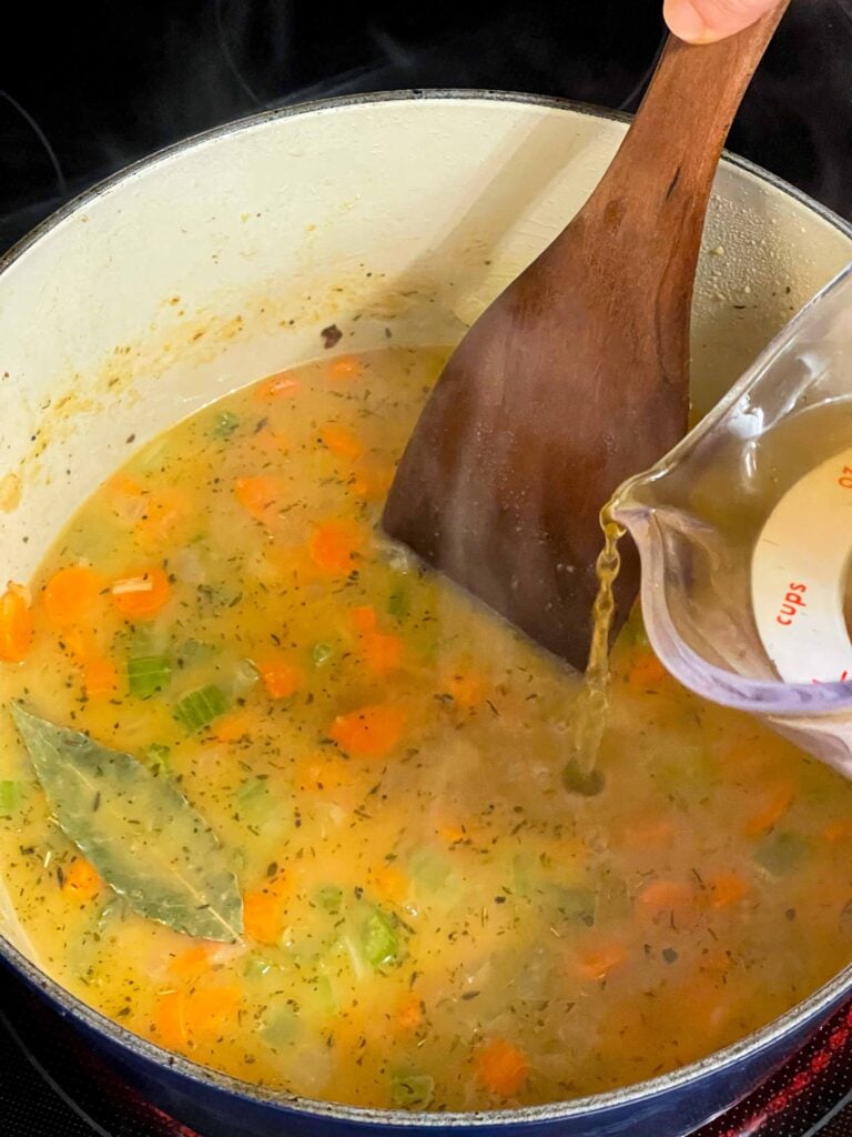 Adding chicken stock to a medley of vegetables in a dutch oven.