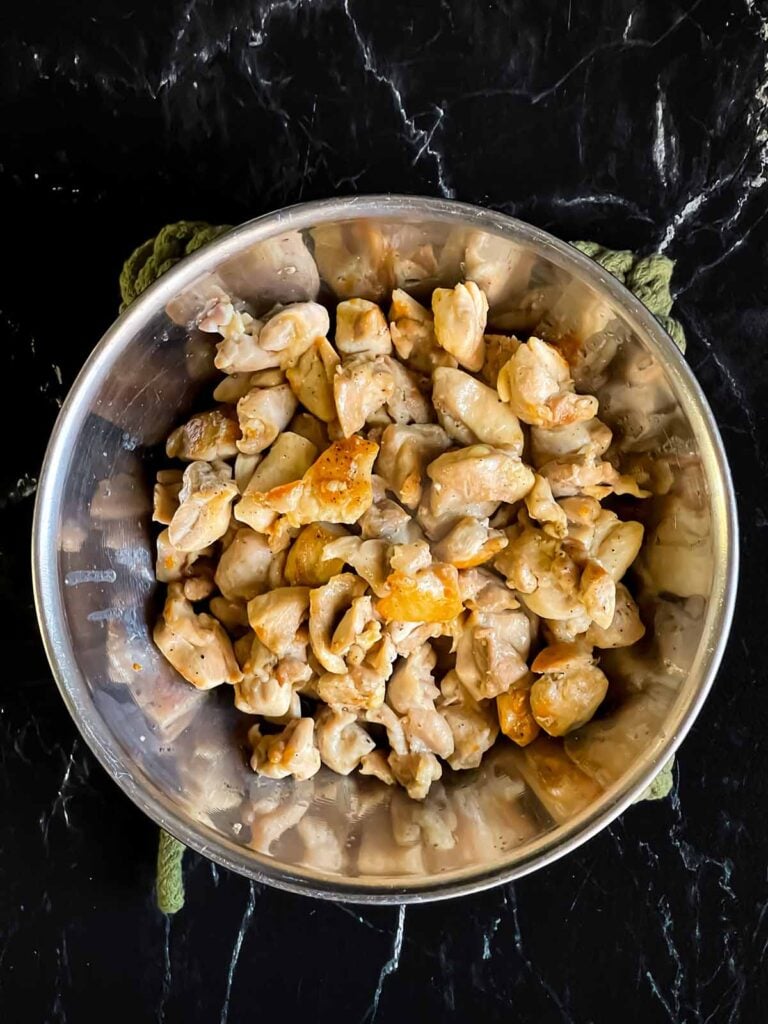 Browned chicken in a stainless steel bowl.