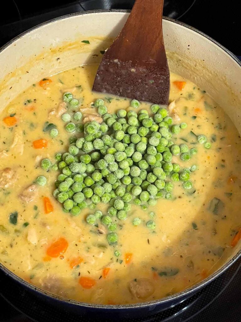 Adding frozen peas to a chicken stew in a dutch oven.
