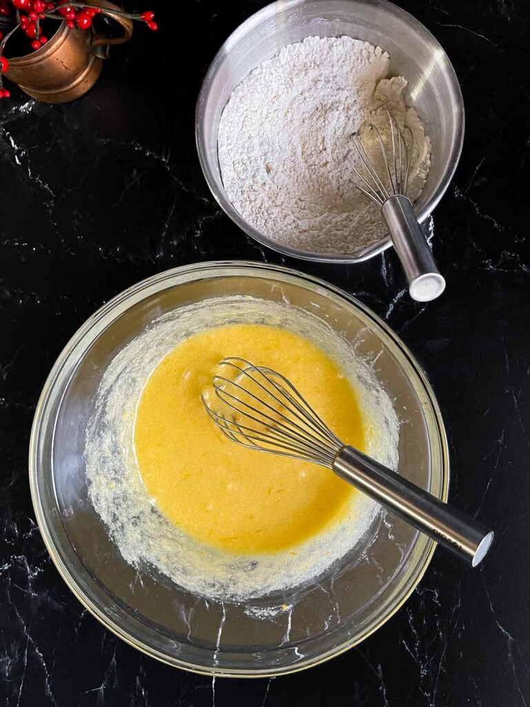 Eggs whisked into the wet ingredients for the cranberry pistachio biscotti in a glass mixing bowl on a dark surface.