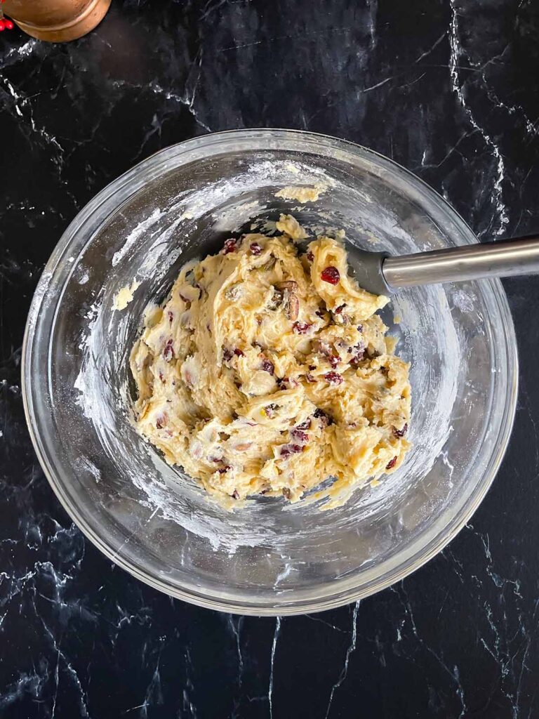 Cranberry pistachio biscotti dough mixed in a glass mixing bowl on a dark surface.