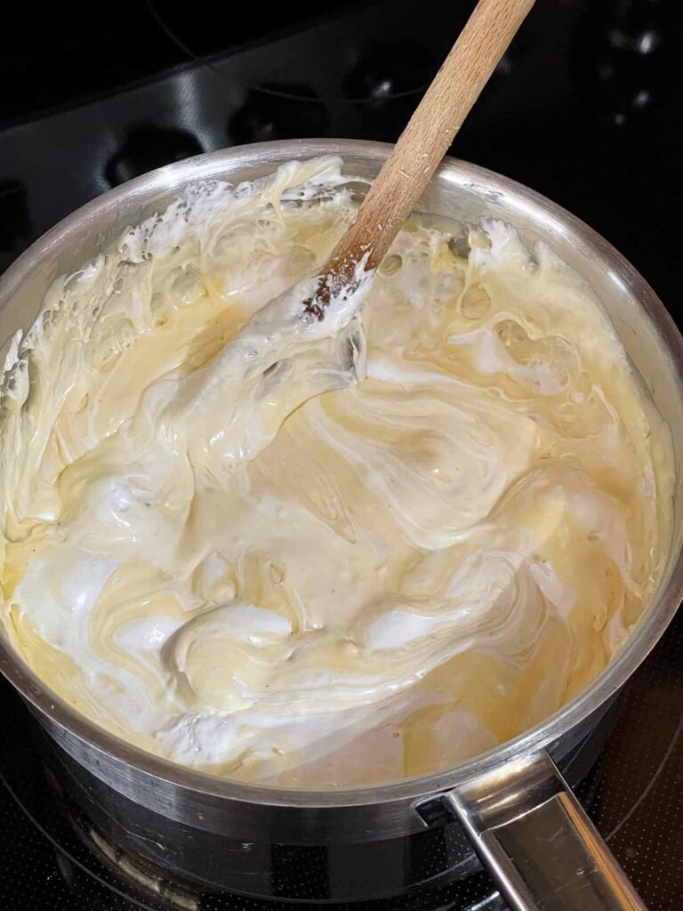 Marshmallow cream added to the eggnog fudge ingredients in a saucepan.