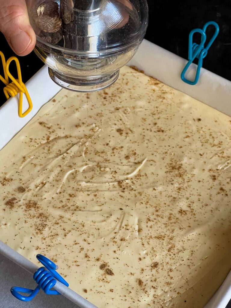 The eggnog fudge poured into the prepared baking pan with a ground nutmeg garnish.