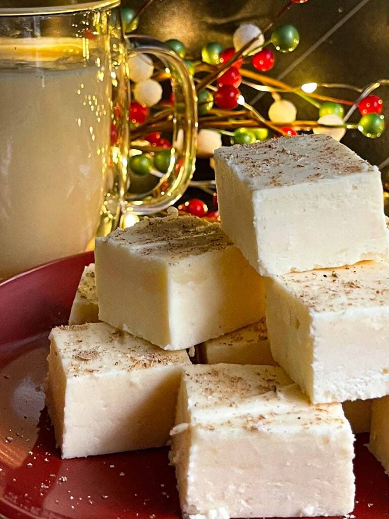 Eggnog fudge on a dark plate with a glass mug of eggnog.