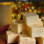 Eggnog fudge stacked on a dark plate with a glass of eggnog.