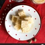 Eggnog fudge stacked on a polka dotted plate with a glass of eggnog and a nutmeg grinder.