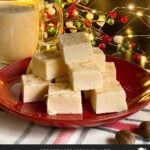 Eggnog fudge stacked on a dark plate with a glass of eggnog.