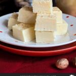 Eggnog fudge stacked on a polka dotted plate with a glass of eggnog and a nutmeg grinder.