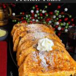 Slices of panettone French toast garnished with powdered sugar, whipped cream, and maple syrup on a dark plate.