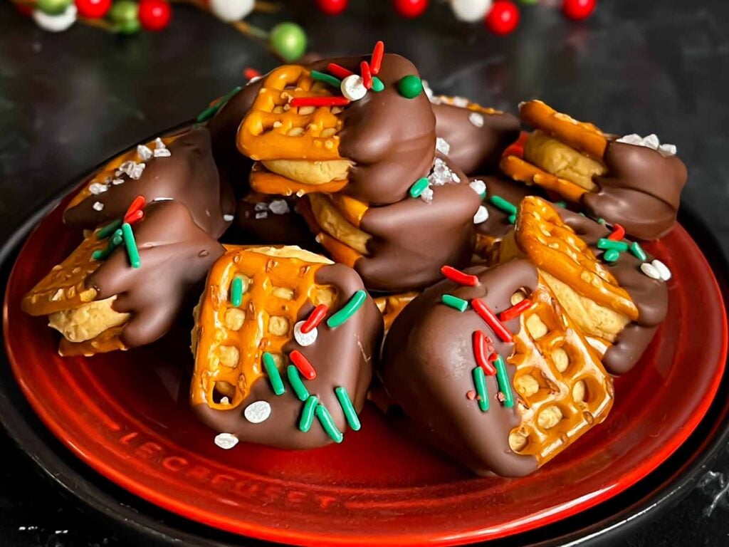 Chocolate covered peanut butter pretzel bites stacked on a dark plate.