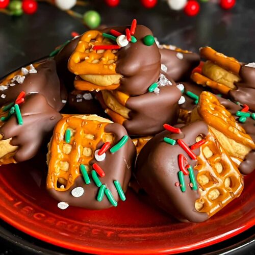 Chocolate covered peanut butter pretzel bites stacked on a dark plate.