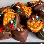 Chocolate covered peanut butter pretzel bites stacked on a parchment paper lined baking sheet.