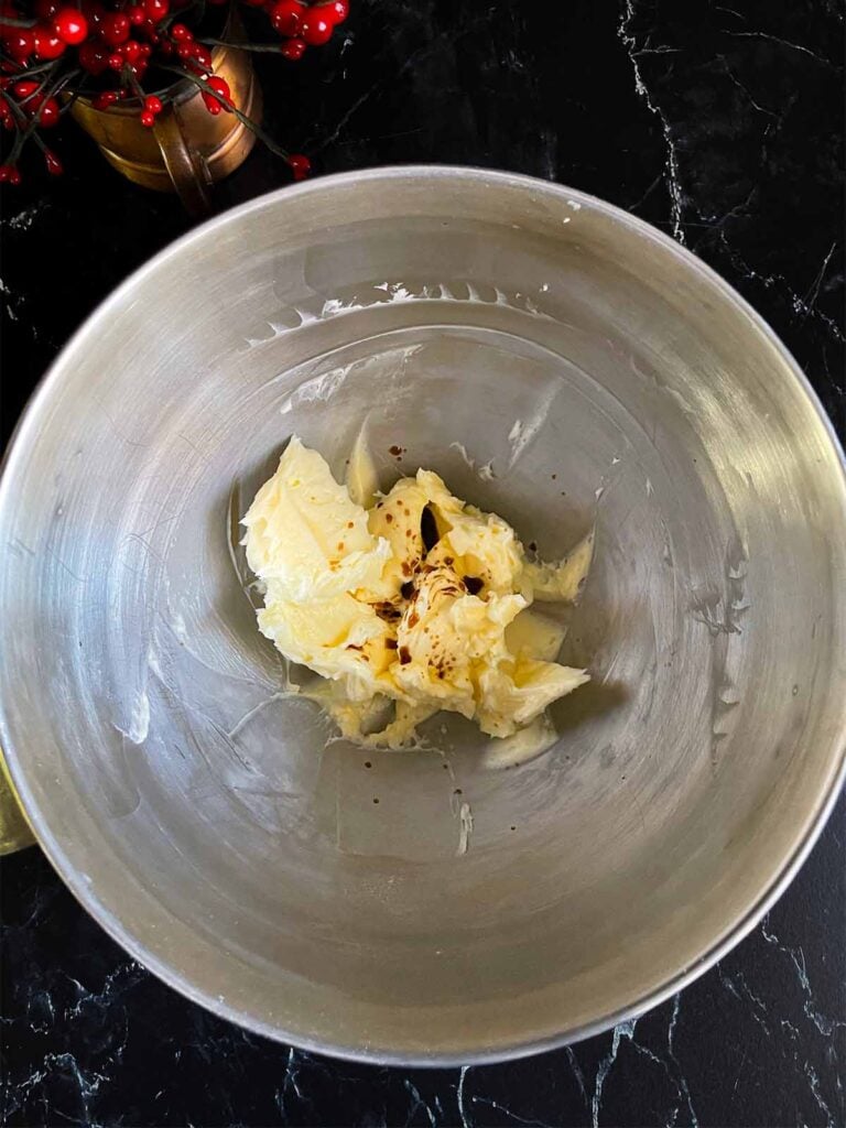 Vanilla added to the whipped butter and powdered sugar in a metal mixing bowl.