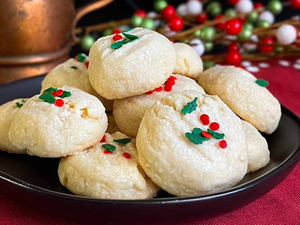 Whipped shortbread cookies stacked on a dark plate.