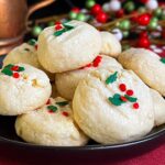 Whipped shortbread cookies stacked on a dark plate.