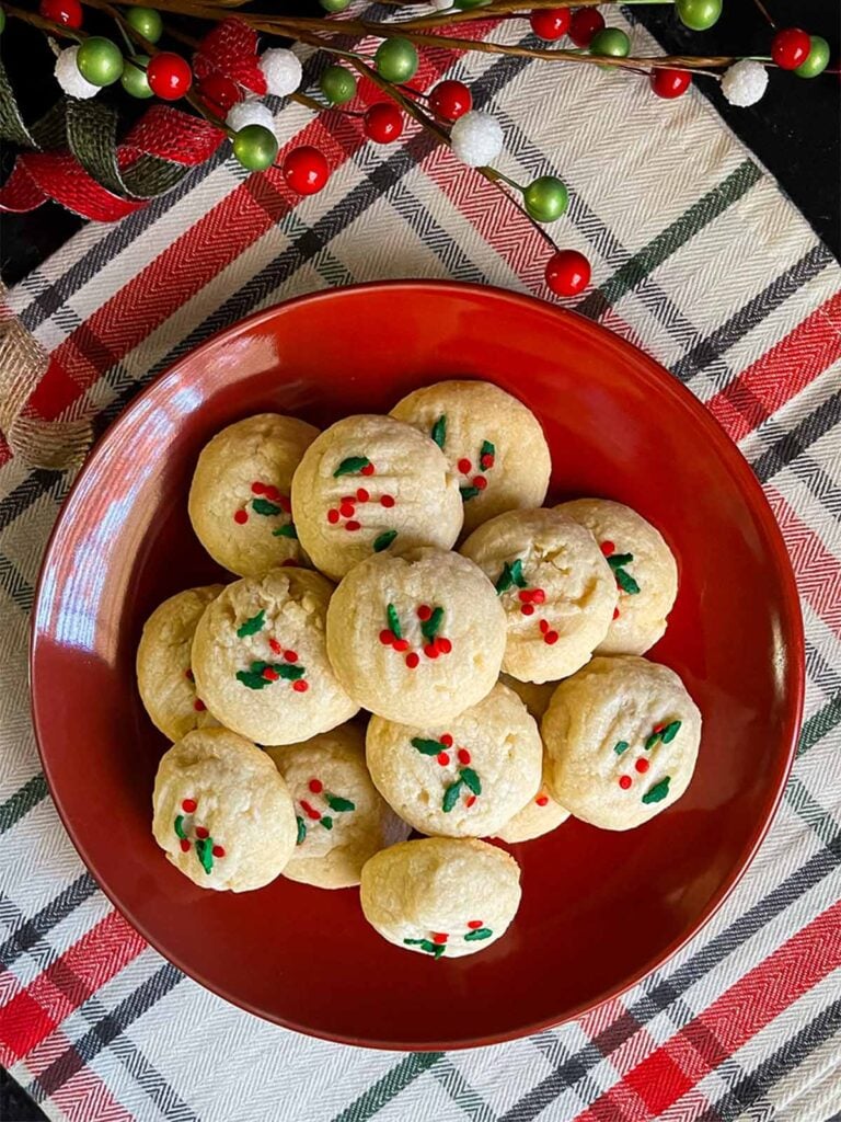 Whipped shortbread cookies stacked on a dark plate.