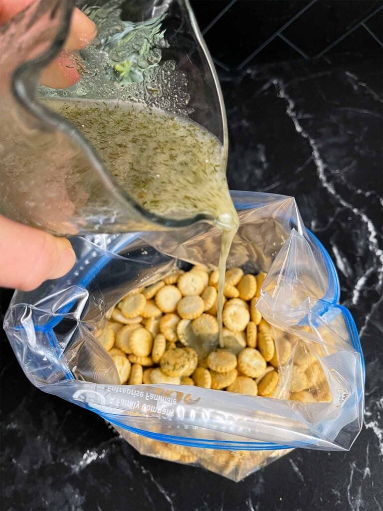 Dill seasoning mixture being poured over the oyster crackers in a resealable plastic bag.