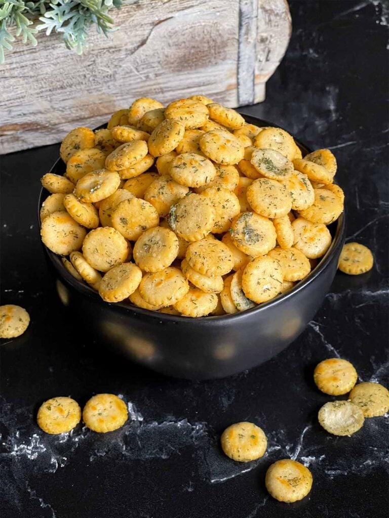 Dill oyster crackers in a dark bowl on a dark surface.