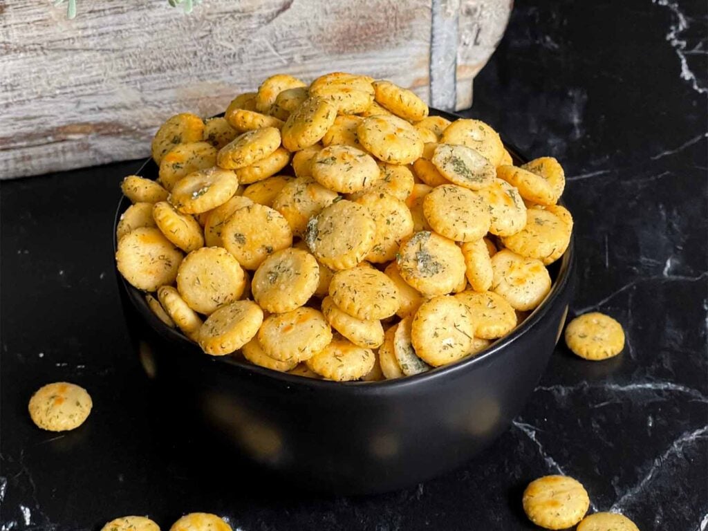 Dill oyster crackers in a dark bowl on a dark surface.