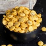 Dill oyster crackers in a dark bowl on a dark surface.