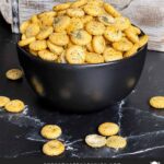 Dill oyster crackers in a dark bowl on a dark surface.