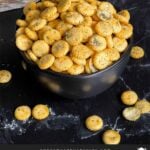 Dill oyster crackers in a dark bowl on a dark surface.