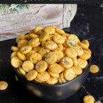 Dill oyster crackers in a dark bowl on a dark surface.