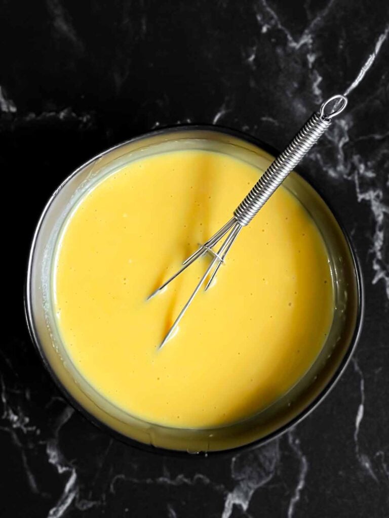 Honey mustard in a dark bowl with a whisk.