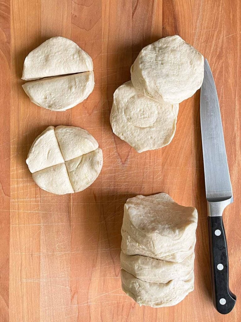 Refrigerated biscuit dough cut into quarters on a wooden board.