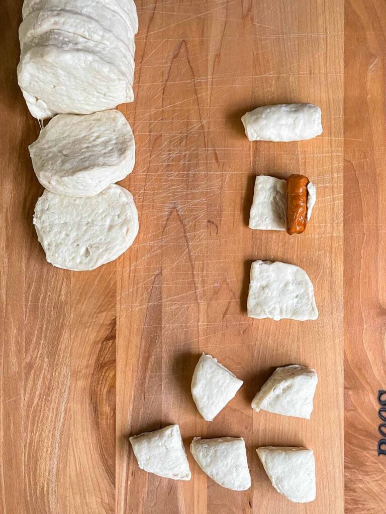 Biscuit dough cut into quarters and being wrapped around a cocktail smokie sausage.