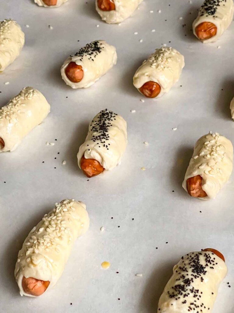 Unbaked pigs in a blanket on a parchment paper lined baking sheet.