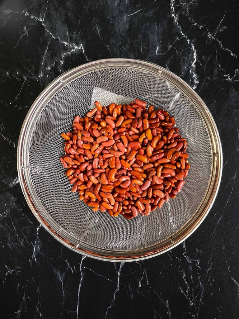 Red beans in a strainer on a dark surface.