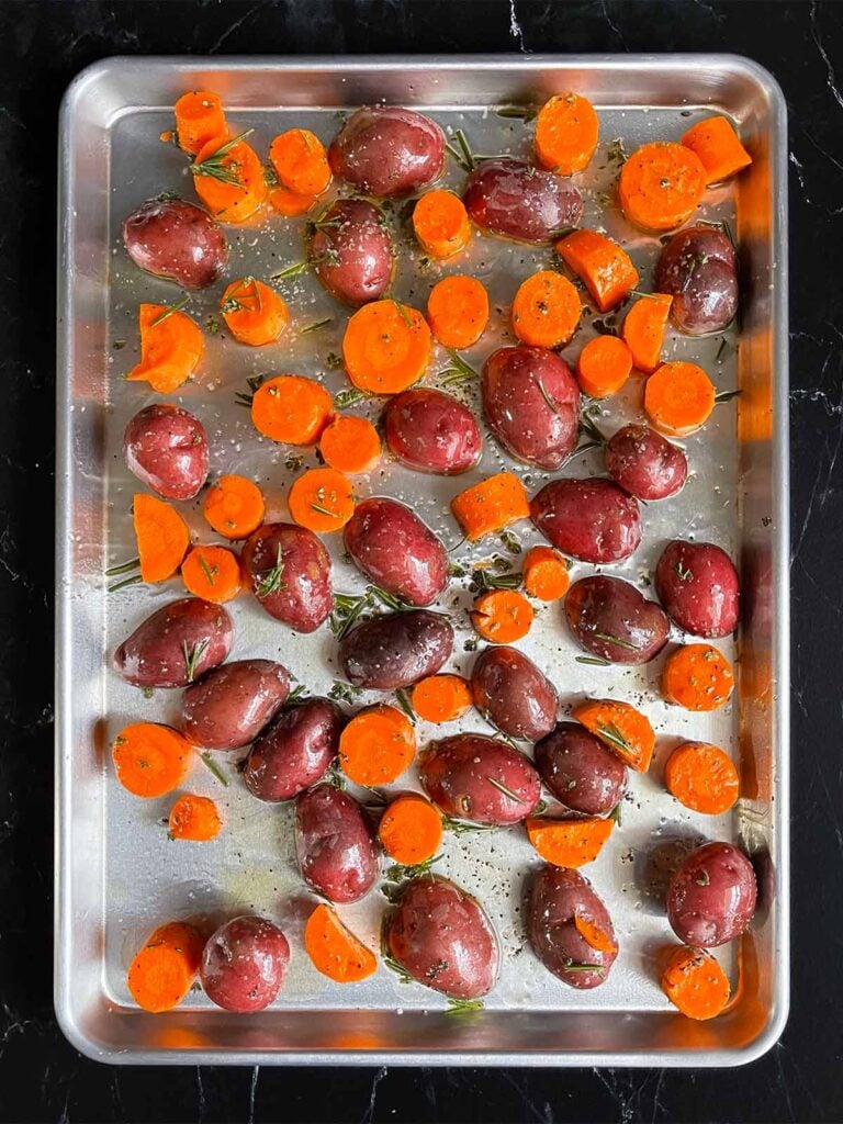 Potatoes and carrots coated with the seasonings, spread into a single layer, on a baking sheet.