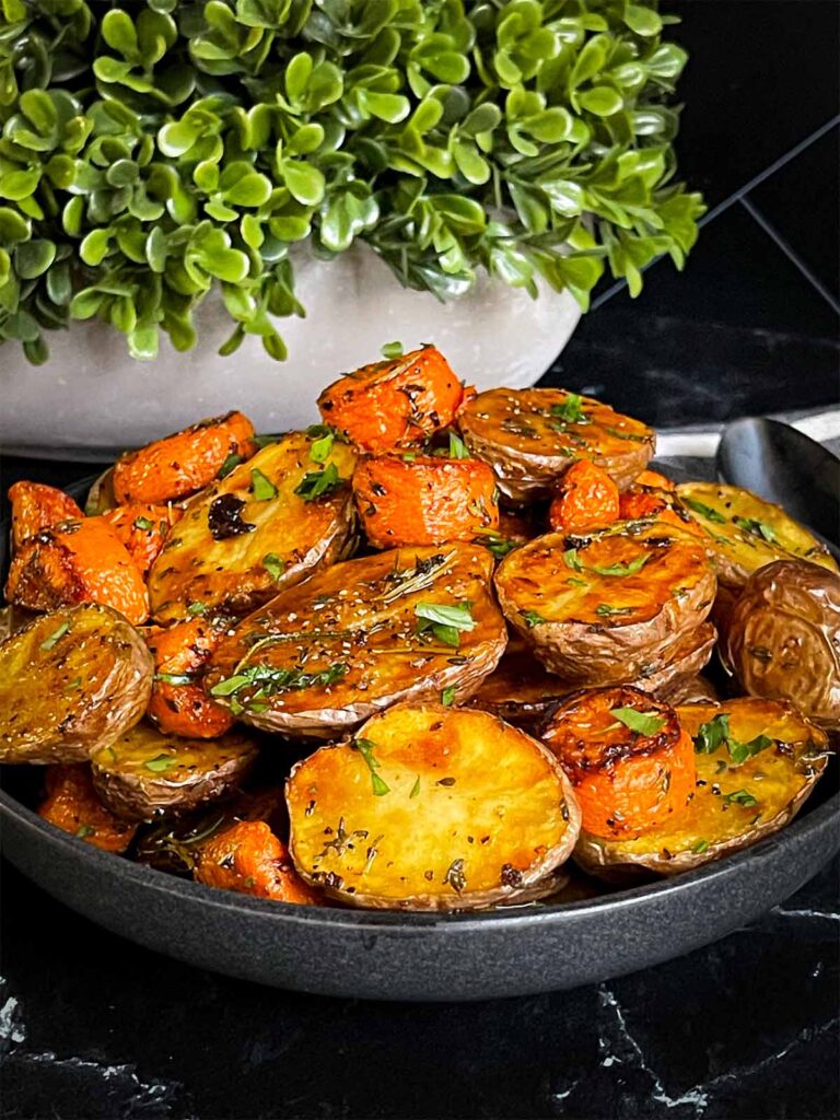 Roasted potatoes and carrots in a dark bowl.