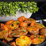 Roasted potatoes and carrots in a dark bowl.