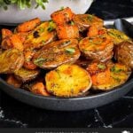 Roasted potatoes and carrots in a dark bowl.