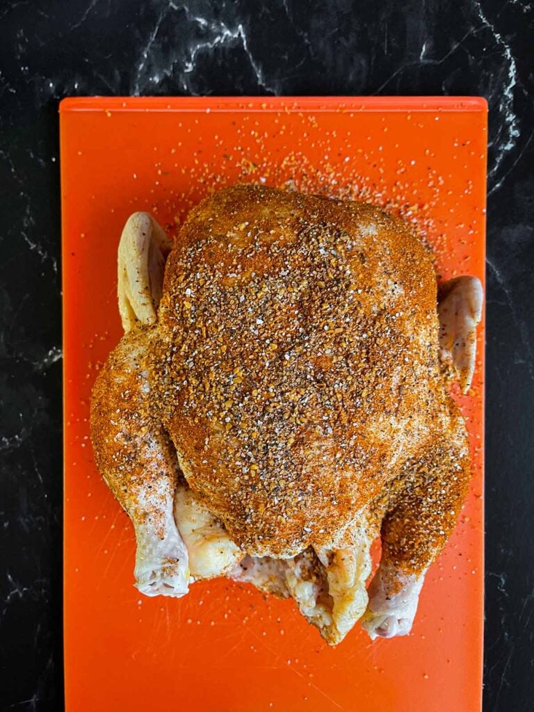 Whole chicken on a plastic cutting board rubbed in spices.