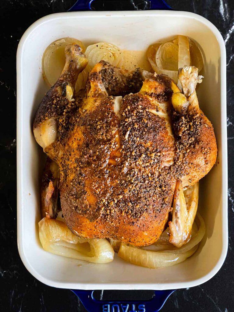 Slow cooker roasted chicken in a serving dish on a dark surface.