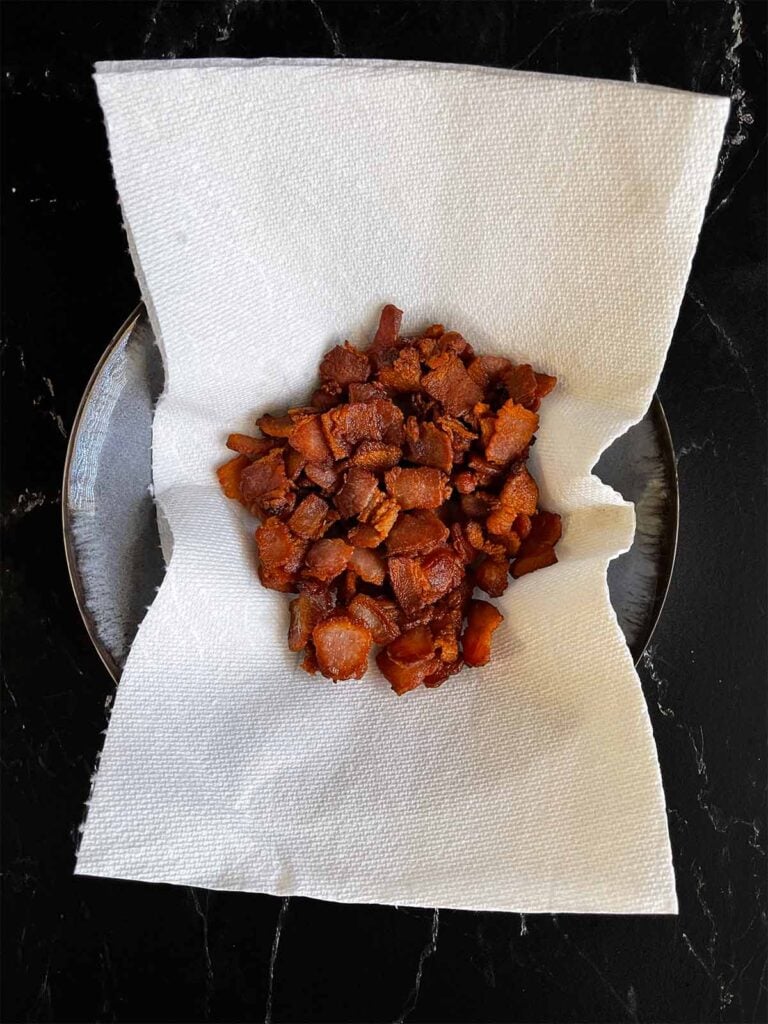 Cooked bacon draining on a paper towel in a bowl.