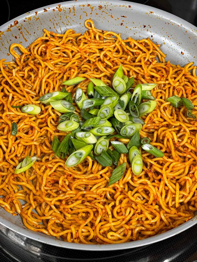 Adding onions to a noodle dish.