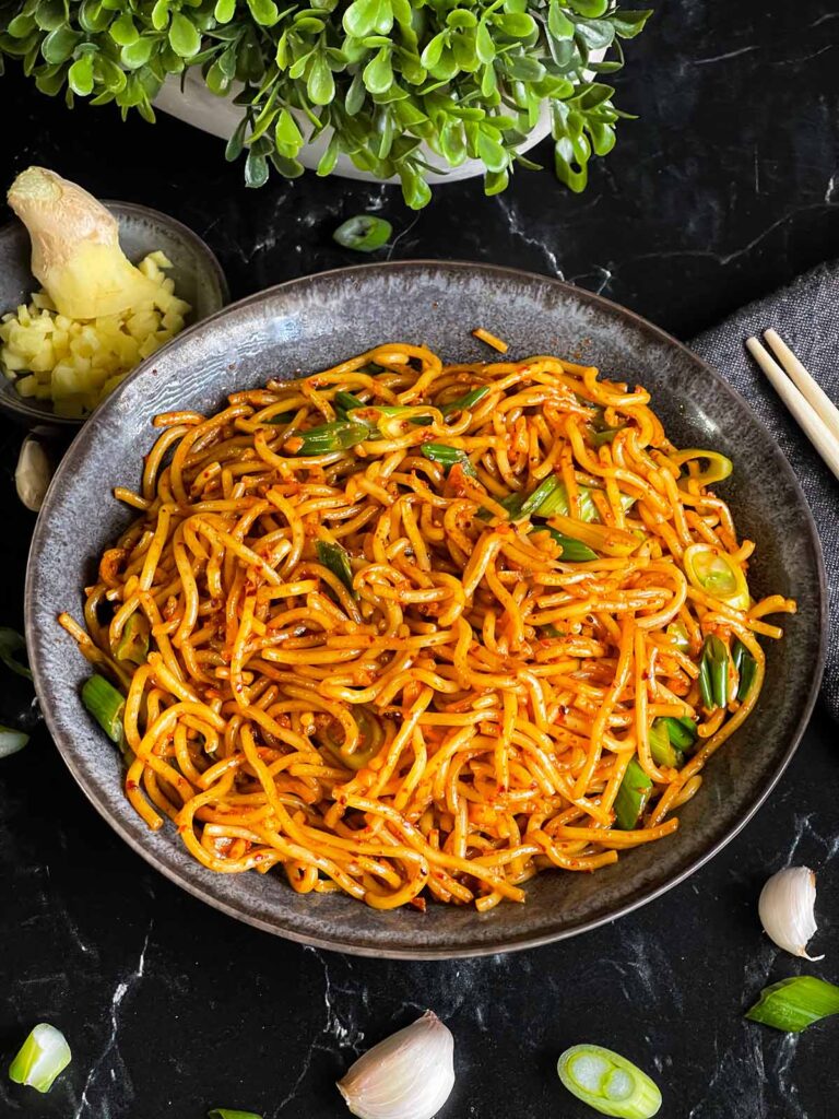 Spicy garlic noodles in a dark bowl.