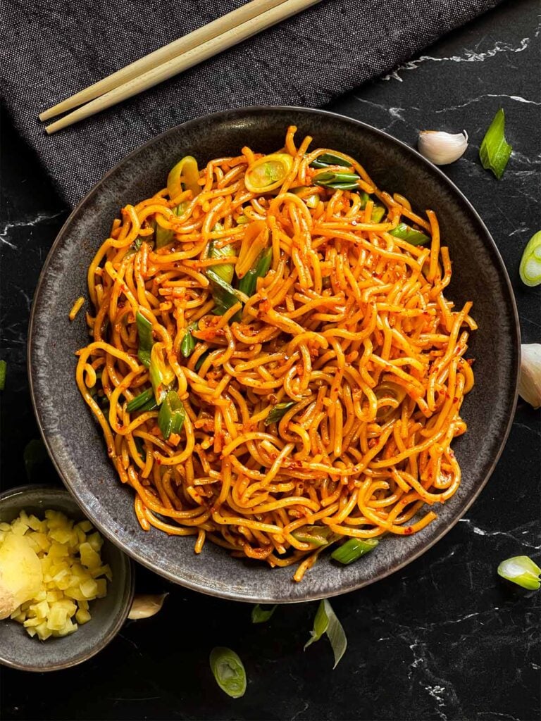 Spicy garlic noodles in a dark bowl.