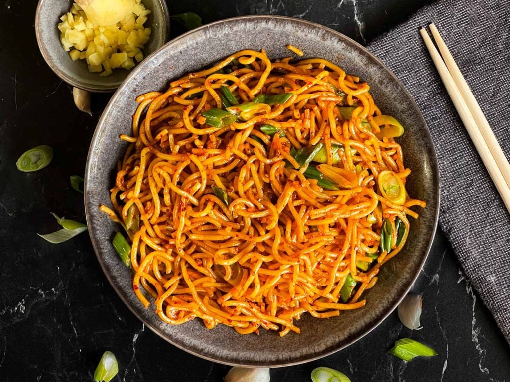 Spicy garlic noodles in a dark bowl.