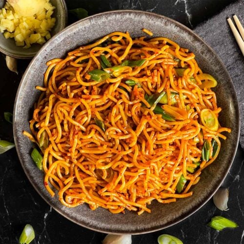 Spicy garlic noodles in a dark bowl.