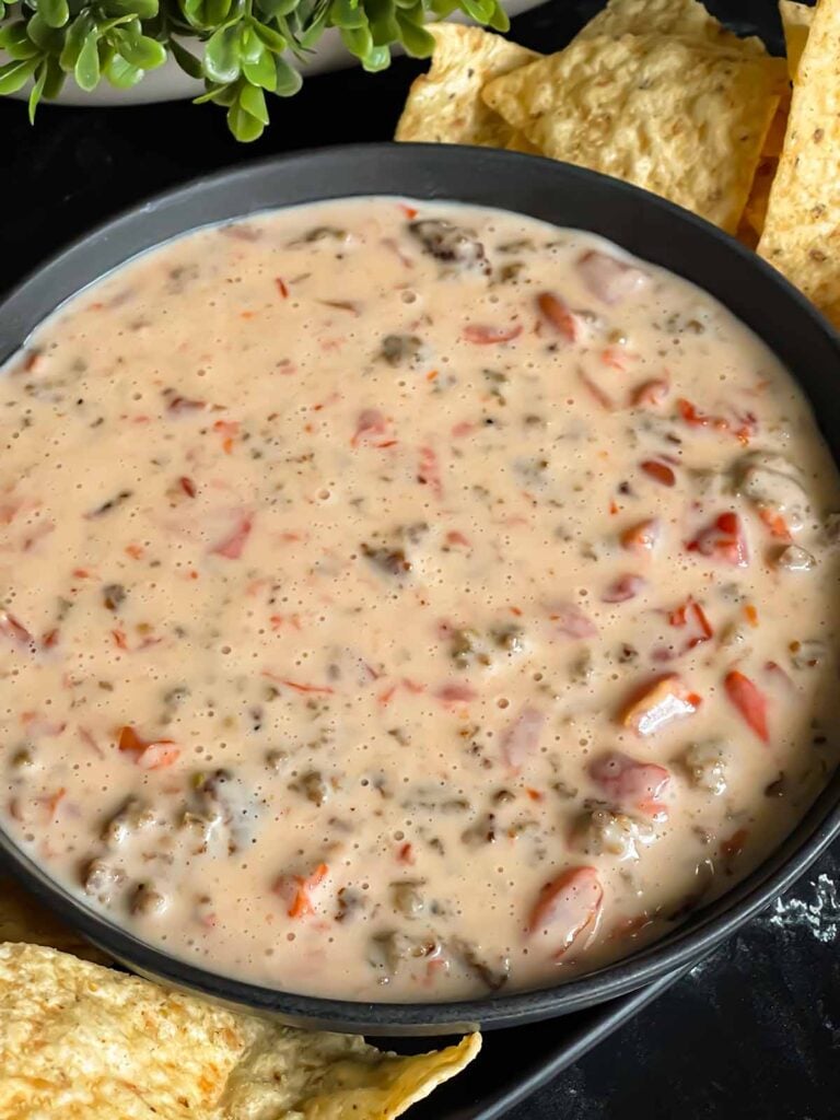 Velveeta cheese dip in a dark bowl with tortilla chips on the side.