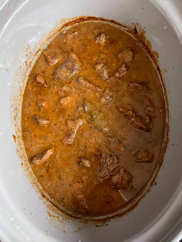 Cooked beef tips and gravy recipe in the crock of a slow cooker.