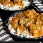 Slow cooker beef tips and gravy over cooked rice on a dark plate on a dark surface.